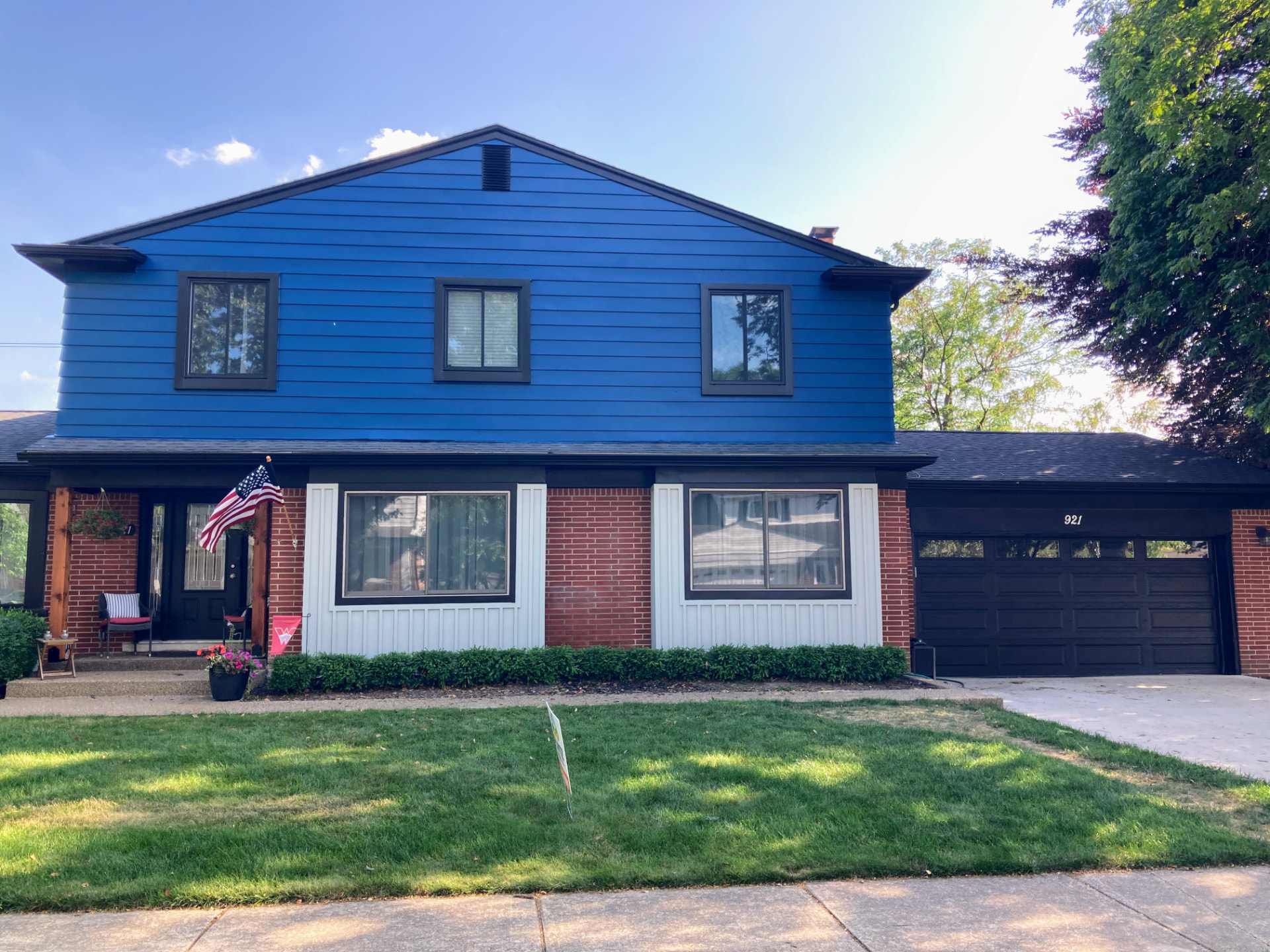 Two-story home with vibrant blue siding, red brick, white trim, and a freshly painted black garage door